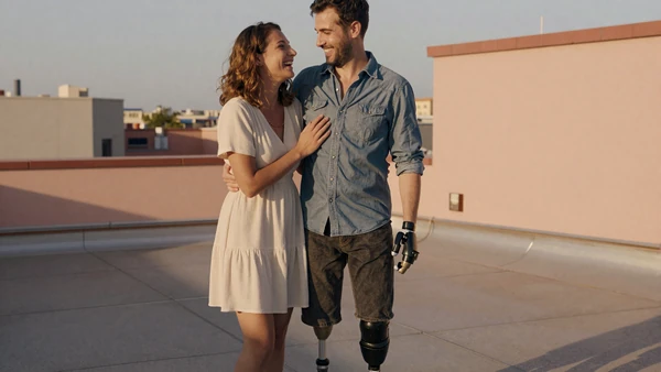 Amputee couple laughing together on a sunlit rooftop at golden hour