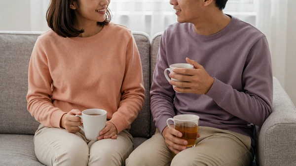 Couple in soft morning light sharing tea and a calm conversation on a living room couch