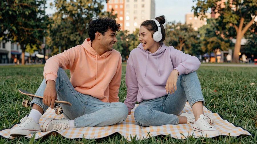 ADHD couple laughing on a park picnic blanket with skateboard and headphones
